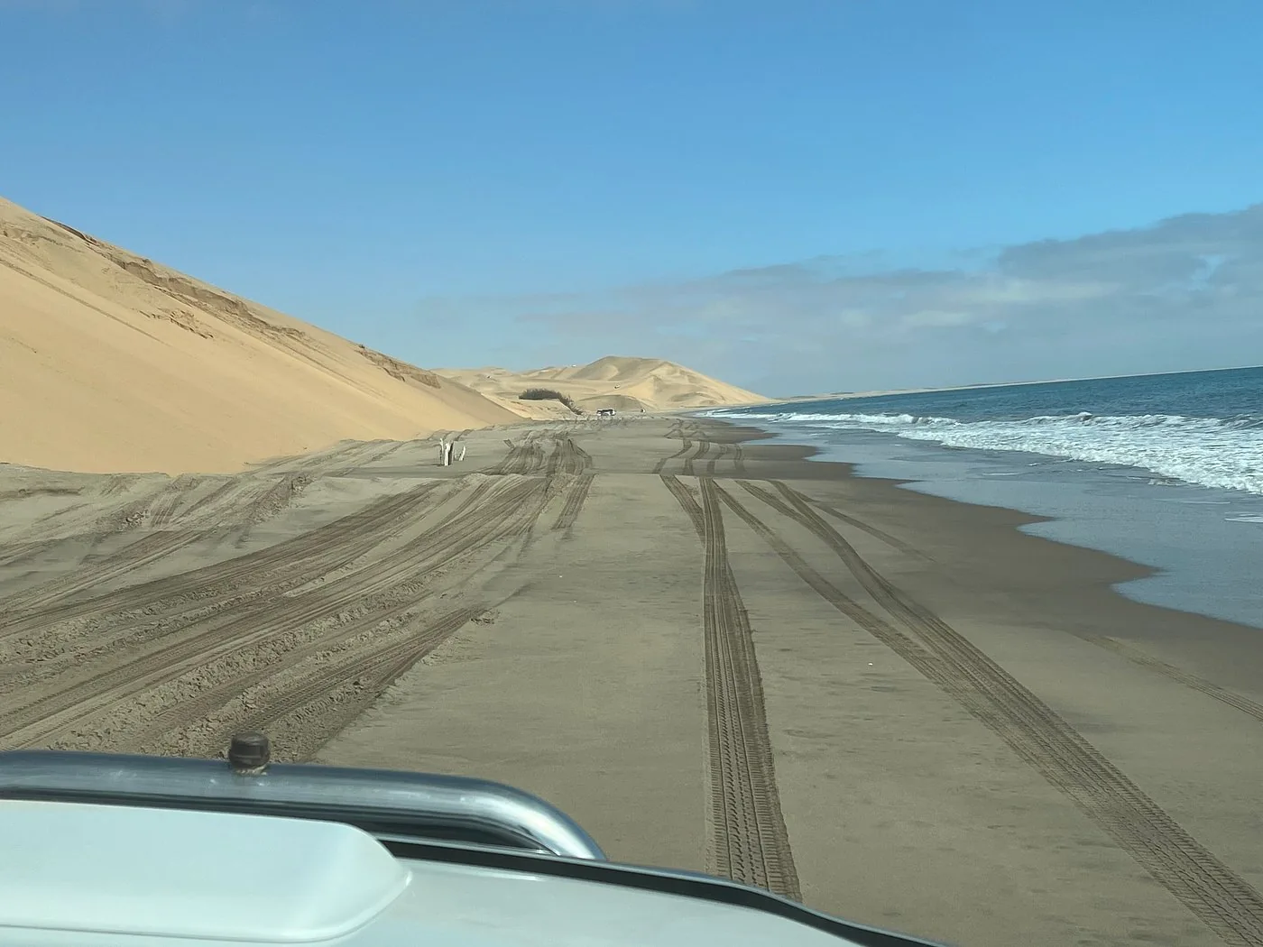 View from a vehicle following tracks between dunes and ocean
