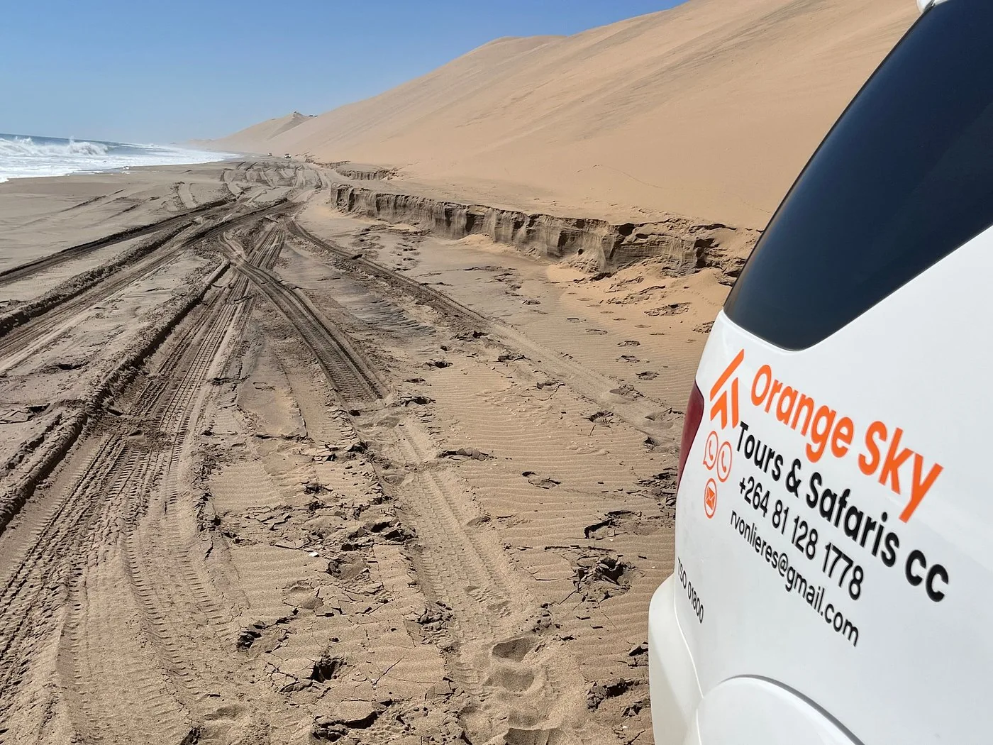 Orange Sky branded vehicle beside coastal dunes and tyre tracks
