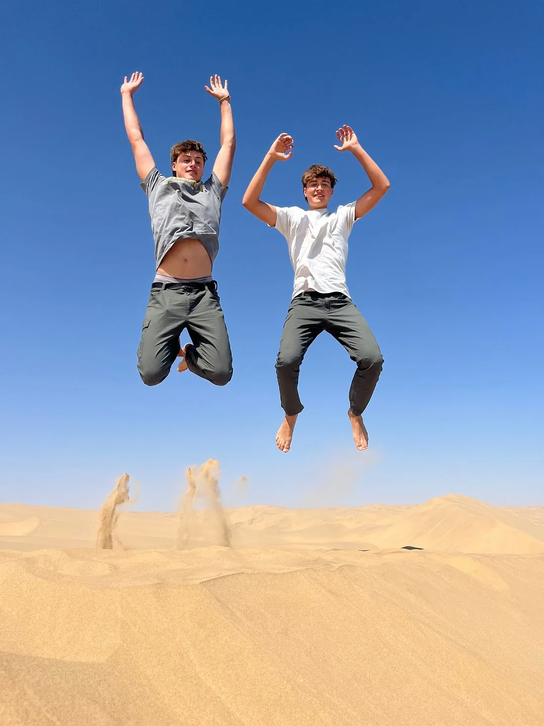 Two guests jumping above a sand dune