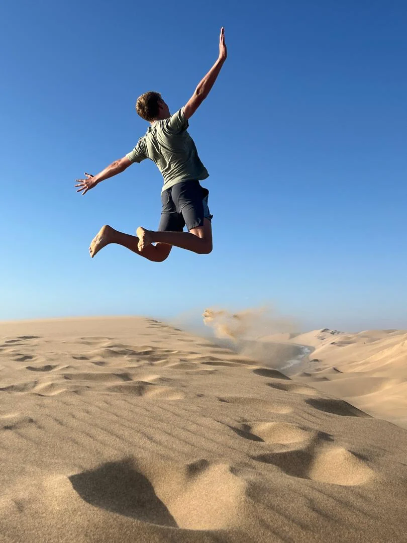 A person jumping in front of coastal dunes